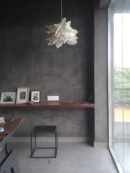 A corner of our Ghitorni studio, featuring grey lime-plastered walls, a simple wooden ledge for displaying art, and a large pivot door that opens the space to the exterior.