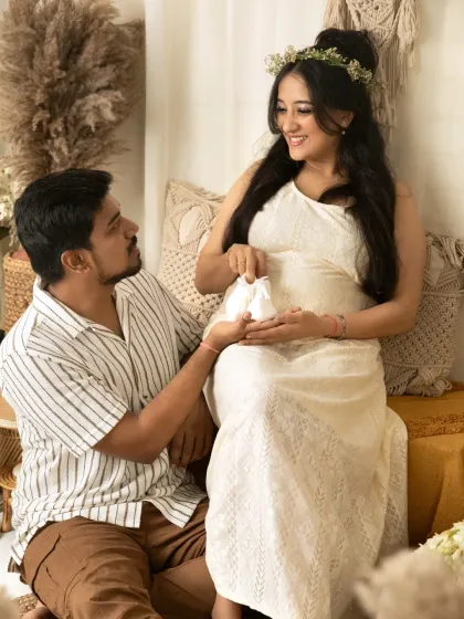 An expecting father lovingly presents a tiny pair of baby shoes to his wife during their maternity photoshoot, symbolizing the new life they are about to welcome.