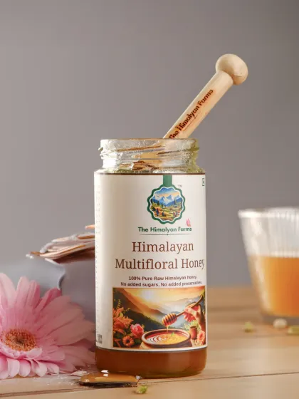 A styled shot of The Himalayan Farms multifloral honey, with a wooden dipper and flowers to create a natural, wholesome feel. The lighting highlights the honey's golden color and texture.