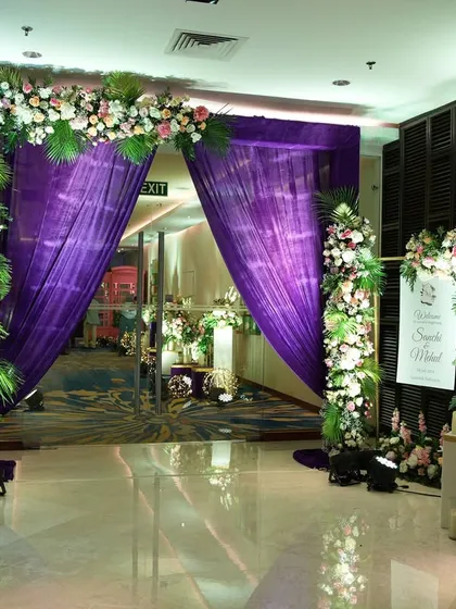 A royal purple entrance, where rich drapes are framed by beautiful floral arrangements, creating a bold and elegant statement for an evening reception.