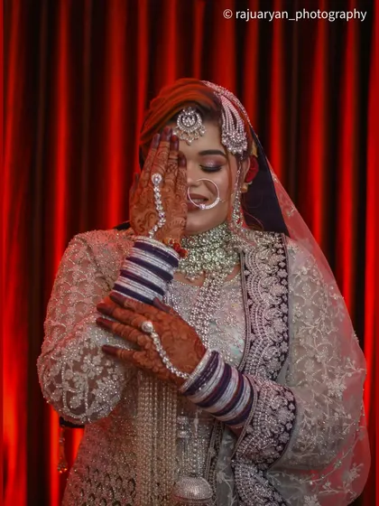 A classic 'haya' or shy pose, beautifully executed. The bride covers half of her face, drawing attention to her expressive eyes and the intricate henna on her hands.