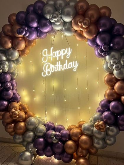 I love working with unique color combinations. This balloon ring uses metallic purple, bronze, and silver balloons, with a 'Happy Birthday' neon sign and fairy lights for a warm and elegant look.