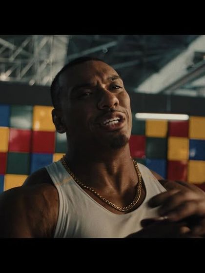 A close-up of Larry Wheels, styled in a classic white tank top and gold chain to create an iconic, old-school strongman look.