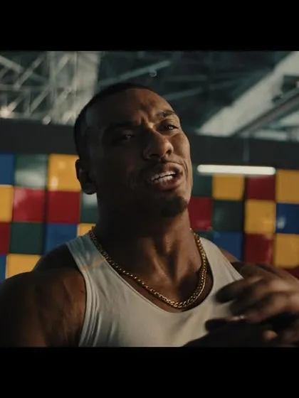 A close-up of Larry Wheels, styled in a classic white tank top and gold chain to create an iconic, old-school strongman look.