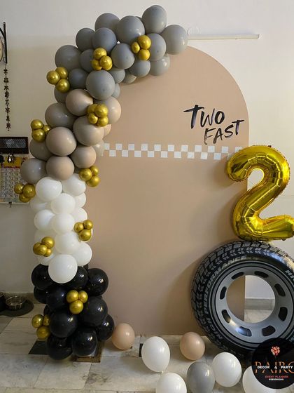A 'Two Fast' car-racing theme for a second birthday, featuring a custom backdrop, a real tire prop, and a balloon arch in a modern color scheme.