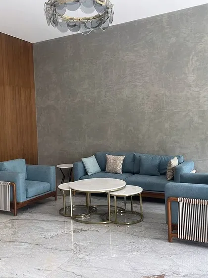 A living room set from the same Tiripur project, featuring a sofa and armchairs with unique woven rope detailing on the arms, paired with a nested set of marble-topped coffee tables.