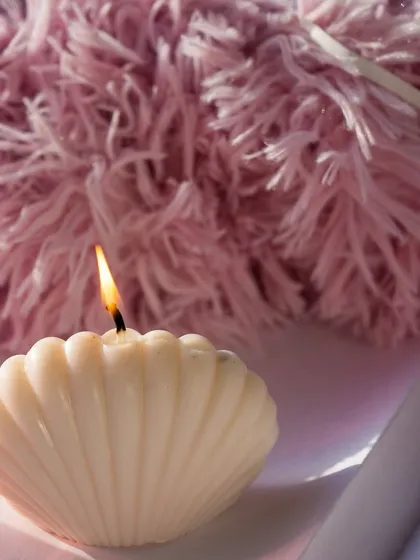 A close-up of our lit oyster shell candle against a fluffy pink background. A perfect weekend mood.