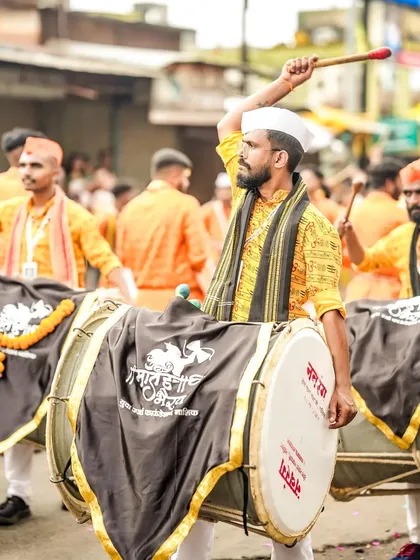 A dhol player in a white cap, his stick raised, leading the rhythm.