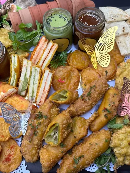 A classic high-tea platter, featuring an assortment of fried snacks like pakoras and spring rolls, alongside chutney sandwiches and dips. Perfect for an afternoon party.