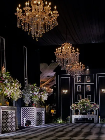 The grandeur of the Sangeet stage, with its dramatic black draping, multiple crystal chandeliers, and elegant white decor elements, ready for a night of performances.