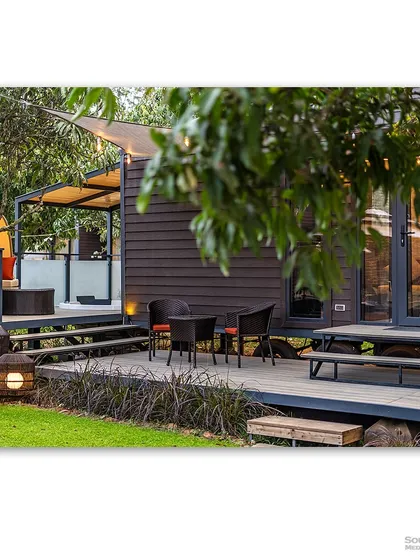 A view of the prefab modular homes at Glamp Wilderness, showing the inviting wooden decks and outdoor seating areas. The image highlights the community feel and the beautiful natural surroundings.