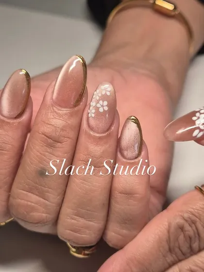 Elegance is in the details. This design features a nude cat-eye polish on almond nails, accented with a fine gold chrome border and delicate, hand-painted white flowers for a sophisticated and chic style.