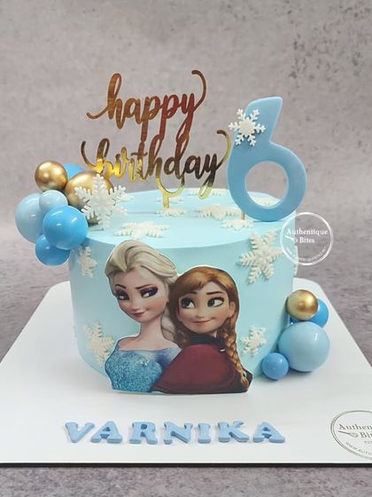 A sweet Frozen cake featuring sisters Elsa and Anna. This light blue cake is decorated with snowflakes and spheres, perfect for a 6th birthday.