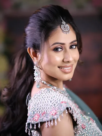 A smiling model wearing a layered zircon necklace with pastel blue stones and a matching maang tikka. This is a fresh and modern take on bridal or festive jewellery.