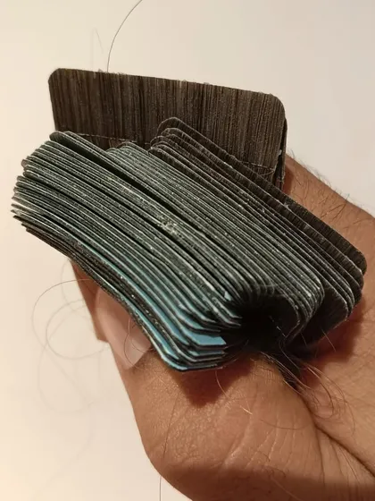 This close-up shot shows a bundle of tape-in extensions ready for application. You can see the thin and discreet tape tabs that lie flat against the head for an undetectable finish.