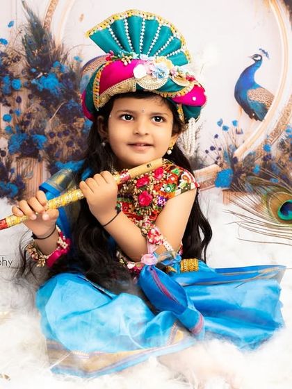 Holding a flute, this little girl looks divine in her Krishna attire. The blue and gold set design creates a rich and heavenly backdrop.