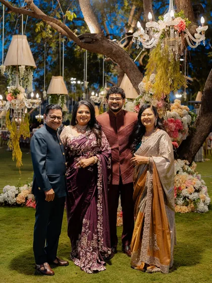 The groom's family looking picture-perfect at the reception. The mother of the groom wears a stunning silver and gold saree, while the father and groom are dressed in complementary bandhgalas.