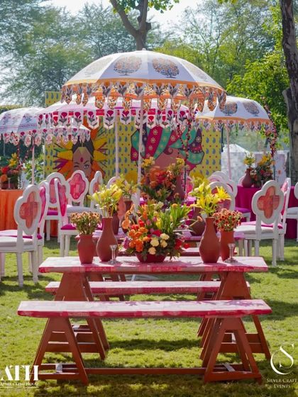 Outdoor seating at a Rajasthani-themed event. The tables and chairs are decorated with block prints, and the area is shaded by beautifully patterned umbrellas, creating a royal and festive ambiance.