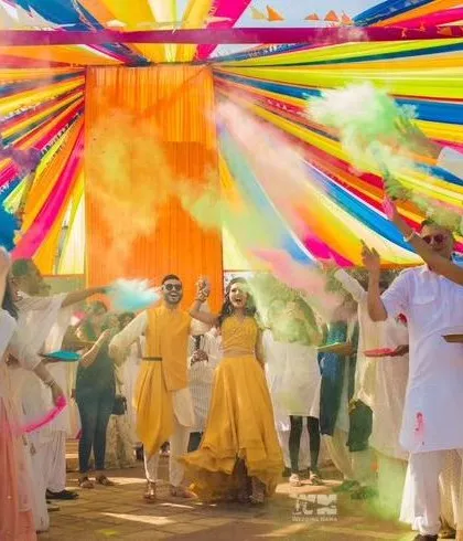 The joy of a Haldi ceremony captured perfectly. The couple celebrates amidst a shower of colorful smoke bombs under a vibrant canopy of drapes, showing how decor can enhance the experience.