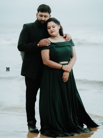 An elegant and moody pre-wedding portrait on the beach. The deep green off-shoulder gown is a sophisticated choice for a romantic evening shoot.