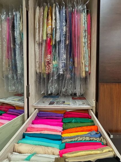 A drawer filled with colorful blouses, file-folded to be seen at a glance. Above, delicate garments are protected in clear covers, showcasing a multi-faceted approach to Indian wear storage.