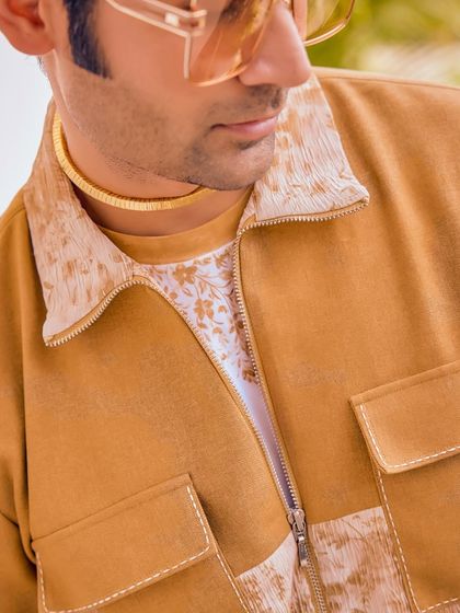 All eyes on subtle glam. This close-up of a mustard jacket from the Sukoon collection shows the delicate floral print on the collar and t-shirt, perfect for cocktail nights.