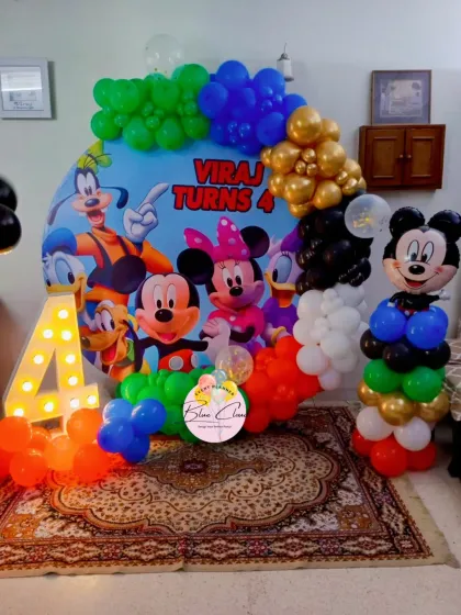 A classic Mickey Mouse Clubhouse theme for a 4th birthday. The decor features a custom character backdrop, a colorful balloon garland, and a Mickey Mouse balloon sculpture.