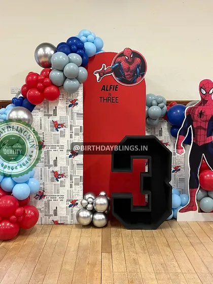 This Spider-Man theme for a third birthday features a life-sized character cutout and a backdrop combining a comic-print panel with a solid red panel. The custom-built number '3' adds a personal touch.