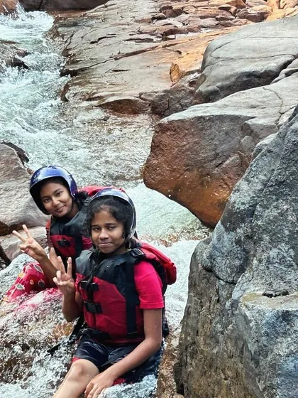 Two friends give peace signs while sitting on the rocks, taking a break from their rafting and kayaking course.