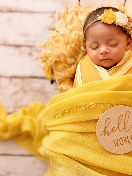 A sweet newborn nestled in a yellow wrap for a sunflower-themed shoot. One-month-olds can be tricky, but with experience, we can still get these beautiful, sleepy shots.