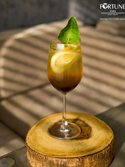 A beautifully crafted cocktail catching the light, served on a rustic wooden coaster at our bar.