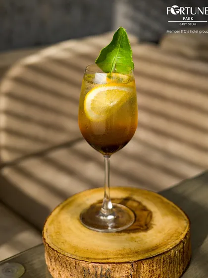 A beautifully crafted cocktail catching the light, served on a rustic wooden coaster at our bar.
