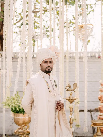 A classic portrait of the groom in his off-white sherwani, standing in front of the beautiful floral decor of his wedding.