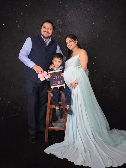 It's a girl! This family portrait is filled with excitement, with the big brother holding a sign and pink shoes to announce his new baby sister. The starry backdrop adds a magical touch.