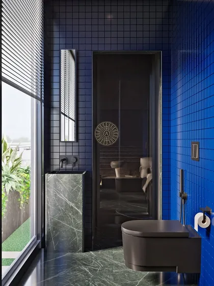 This guest bathroom in a Kolkata home is defined by its bold color and material choices. Deep blue grid tiles cover the walls, contrasted with green marble flooring and a green marble pedestal sink. Matte black fixtures complete the modern look.