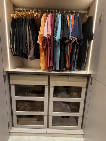 A compact but mighty wardrobe section. Colorful t-shirts are hung above a bank of drawers with glass fronts, offering a mix of visible and concealed storage.