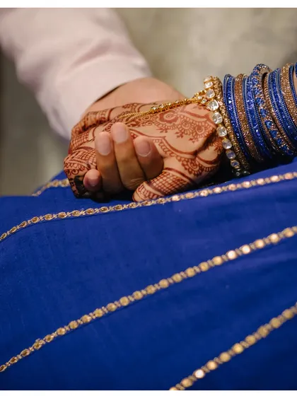 A close-up of the couple holding hands, a simple yet powerful symbol of their union. The intricate henna and the blue of her bangles add to the beauty of this intimate shot.