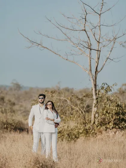 A powerful, minimalist shot of the couple in matching white suits in a field in Goa. The stark tree and dry grass create a unique, high-fashion backdrop.