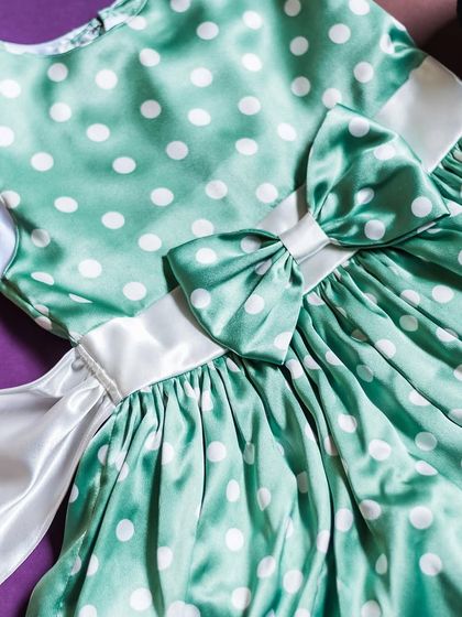 This mint green polka dot dress is made from a beautiful, lustrous satin. The crisp white sash and bow provide a lovely contrast and an elegant finish.