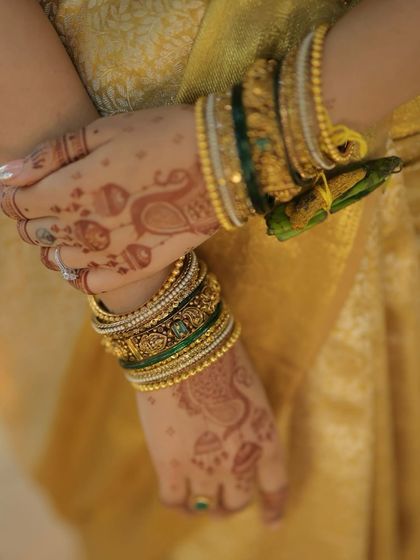 A close-up of the bride's hands, adorned with intricate mehndi and traditional green and gold bangles, an essential part of the South Indian bridal look.