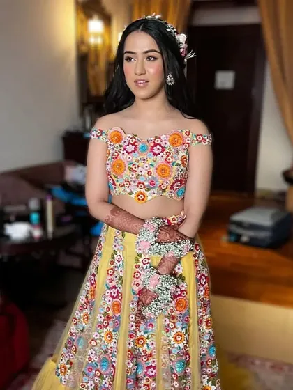 A bride ready for her Mehendi ceremony with her hair in soft waves, adorned with a rustic floral crown. This is a fresh and natural look that is both beautiful and comfortable.