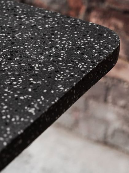 A close-up of the edge of the terrazzo cafe tabletop, revealing the density of the aggregate and the smooth, curved finish of the corner.