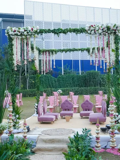 For a fresh and romantic daytime wedding, I designed this garden mandap using a vibrant pink and green palette. The structure is covered in greenery, with hanging floral strings of rajnigandha and roses, and traditional bells for a touch of South Indian charm.