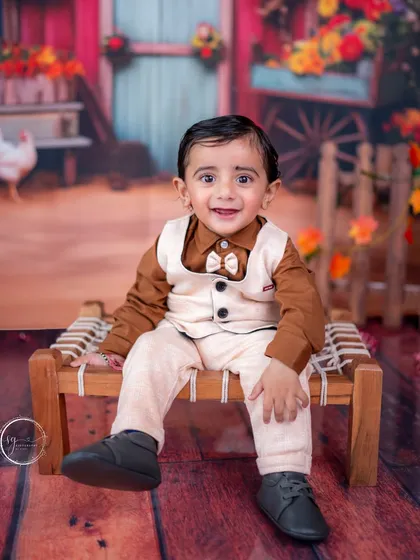 This little boy looks charming in his vest and bow tie, seated on a miniature charpai for a rustic, barnyard-themed shoot.