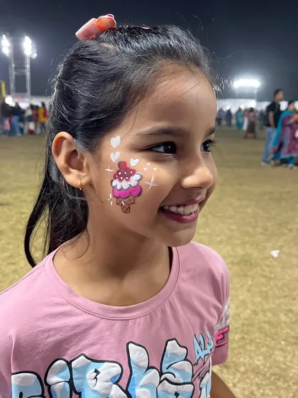 A happy girl with a sweet ice cream cone painted on her cheek at a school funfair. Face painting always adds a touch of magic and fun to any kids' event.