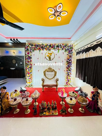 A wide view of the floral home baby shower decor, showing the complete setup with the ornate chair and traditional plate arrangements on a red carpet.