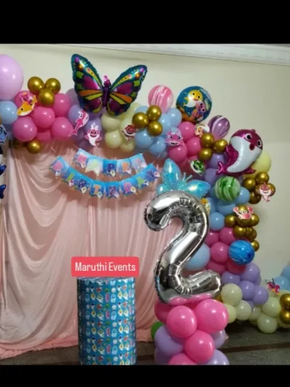 A Baby Shark party for a 2nd birthday, featuring a pink curtain backdrop and a balloon garland with character and butterfly foil balloons.