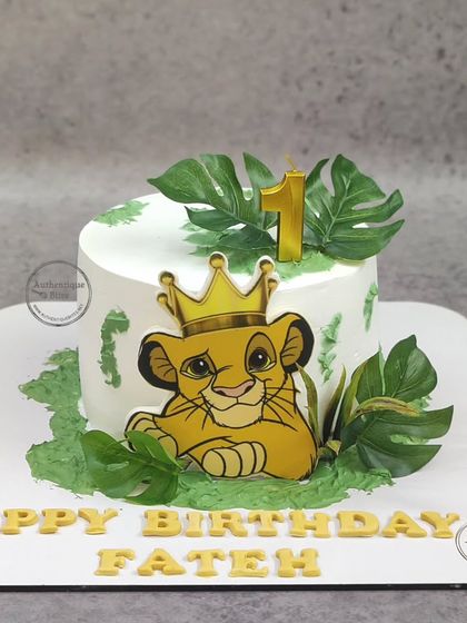 A Simba-themed cake for a first birthday. This Lion King cake features a cute Simba with a crown, surrounded by jungle leaves.