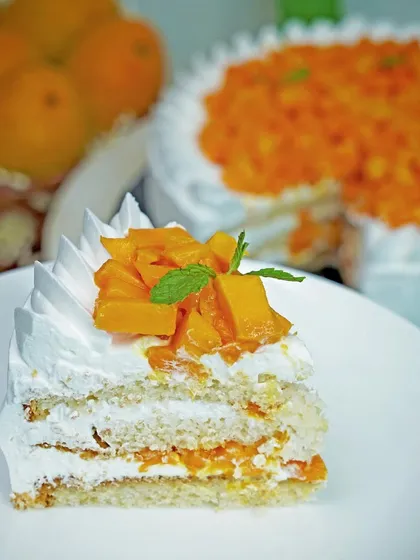 A perfect slice of fresh mango cake on a white plate, showing the layers of cream and fruit. This classic food shot highlights the freshness and texture of the dessert.