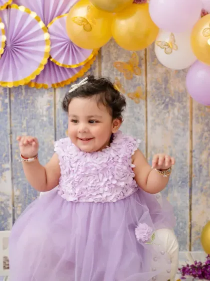 Pure happiness. This baby girl's joyful expression is perfectly framed by a beautiful arch of lavender and gold balloons for her first birthday.
